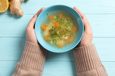 Sick woman holding bowl of fresh homemade soup to cure flu at table, top viewの写真素材