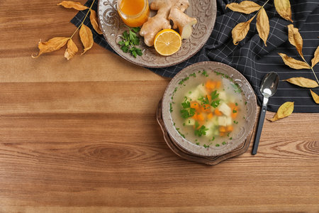 Flat lay composition with bowl of fresh homemade soup to cure flu and space for text on wooden backgroundの写真素材