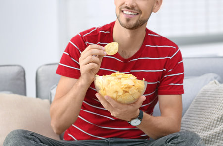 Man with bowl of potato chips sitting on sofa, closeupの写真素材