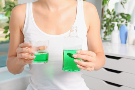 Woman holding bottle and glass with mouthwash in bathroom, closeup. Teeth careの写真素材