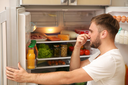 Young man holding nose cause of bad smell in refrigerator at homeの写真素材