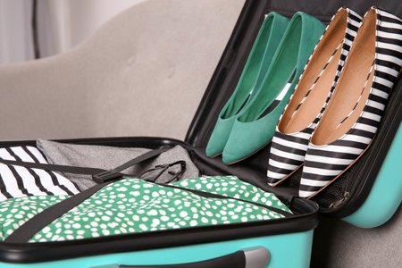 Modern suitcase with clothes and shoes on sofa indoors