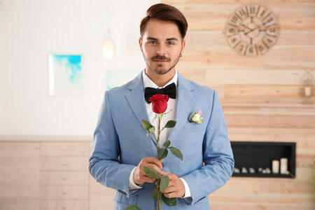 Handsome man in formal wear holding red rose indoorsの写真素材