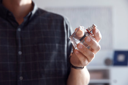 Young man with bottle of perfume indoors, closeupの写真素材