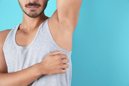 Young man showing armpit on color background, space for text. Using deodorantの写真素材