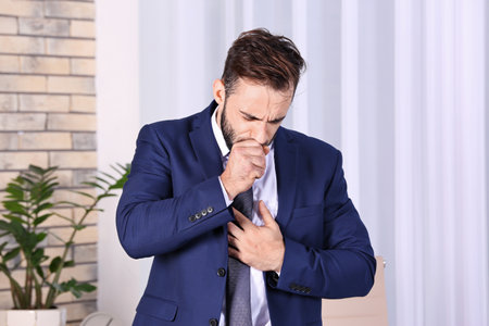 Ill businessman suffering from cough in officeの写真素材