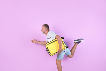 Senior man with suitcase running on color background. vacation travelの写真素材