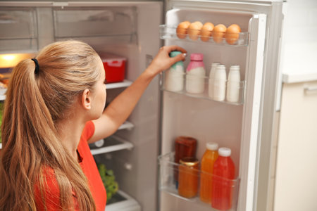 Young woman taking yogurt from refrigerator at homeの写真素材