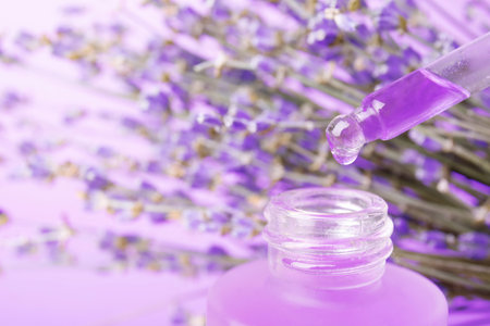 Dripping natural lavender oil into bottle against blurred background, closeup. Space for textの写真素材