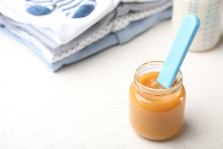 Jar with baby food and clothes on light table. Space for textの写真素材