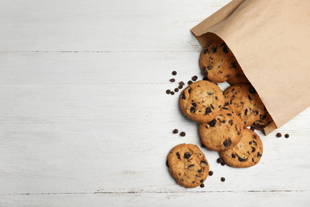 Paper bag with delicious chocolate chip cookies on wooden table, flat lay. Space for textの写真素材