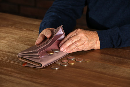 Poor elderly woman counting coins at table, focus on hands