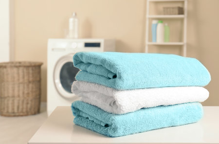 Stack of clean soft towels on table in laundry room. Space for textの写真素材