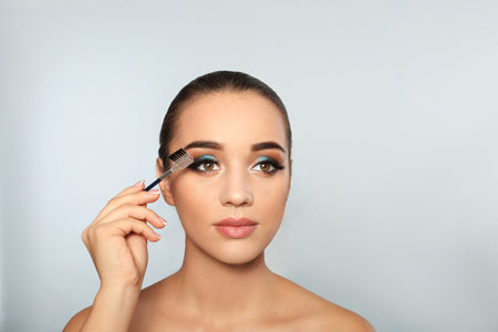Portrait of young woman with eyelash extensions holding brush on light backgroundの写真素材