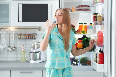 Woman drinking water out of bottle near refrigerator in kitchenの写真素材