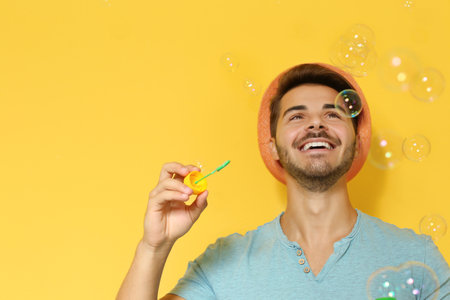 Young man blowing soap bubbles on color background. Space for textの写真素材