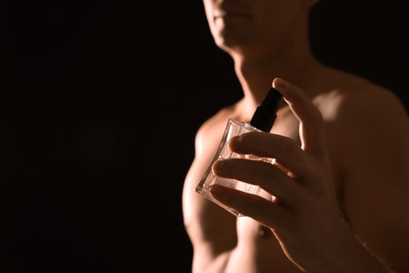 Young man with perfume bottle on black background, closeup. Space for textの写真素材