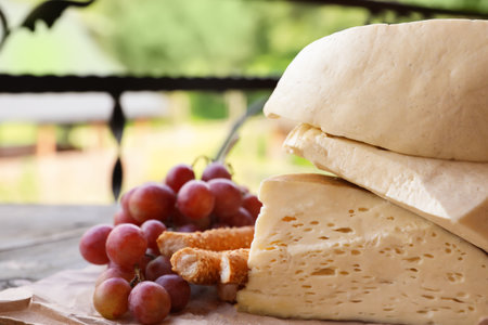 Delicious cheese, bread and ripe grapes on wooden table, closeup