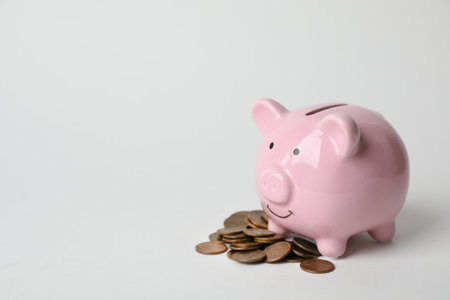 Cute piggy bank and coins on light background. Space for textの写真素材