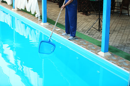 Male worker cleaning outdoor pool with scoop netの写真素材