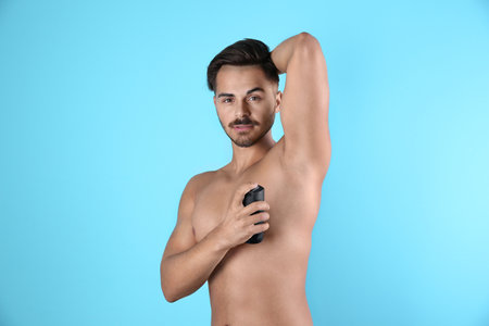 Young man using deodorant on color backgroundの写真素材