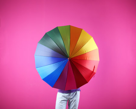 Man hiding behind rainbow umbrella on color backgroundの写真素材
