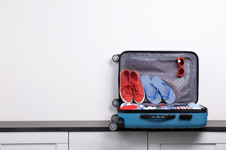 Packed suitcase with clothes and shoes on chest of drawers indoors. Space for text