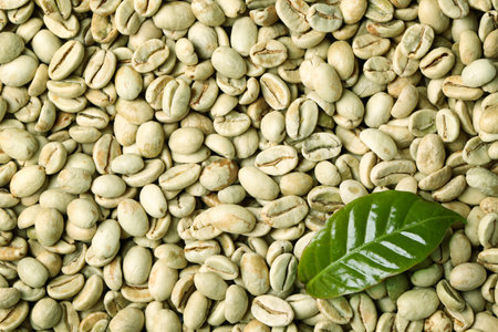 Green coffee beans and fresh leaves as background, top view