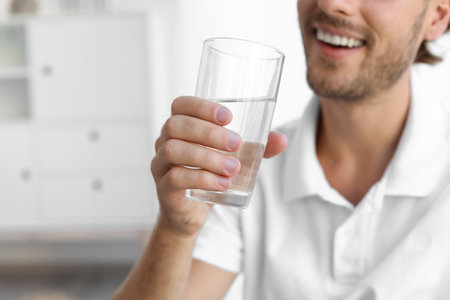 Young man holding glass of clean water indoors, closeup. Space for textの写真素材
