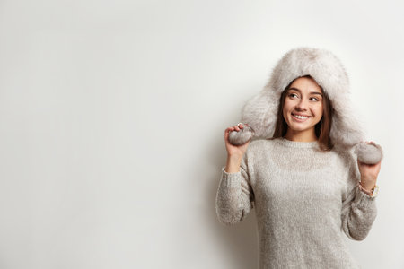 Beautiful young woman in warm sweater with fur hat on white background. Space for textの写真素材