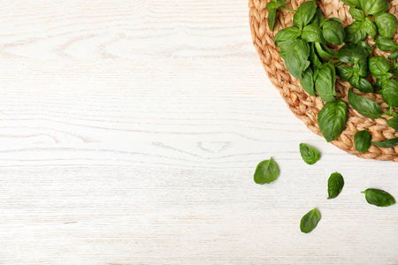 Wicker mat and fresh basil leaves on table, top view with space for textの写真素材