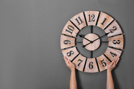 Woman holding clock near gray wall, space for text