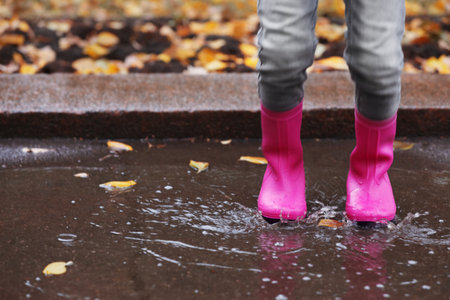 Little girl wearing rubber boots splashing in puddle on rainy day, focus of legs. autumn walkの写真素材
