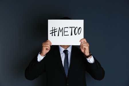Man holding paper with text "#METOO" on dark background. Problem of sexual harassment at workの写真素材