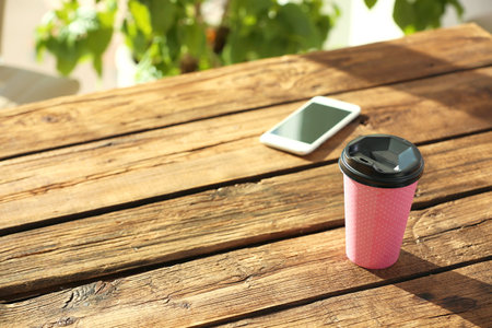 Cardboard cup of coffee and mobile phone on wooden tableの写真素材