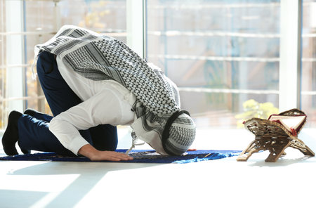 Muslim man with Koran praying on rug indoorsの写真素材