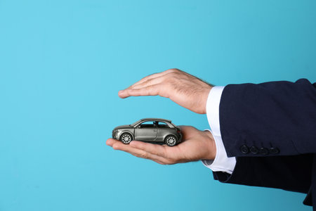 Male insurance agent holding toy car on color background, closeup. Space for textの写真素材