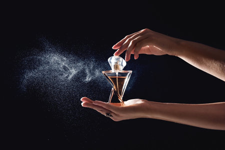 Young woman spraying perfume on black background, closeup