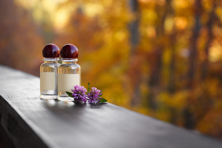 Bottles with essential oil and flowers on blurred background. Space for text