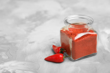 Jar of chili pepper powder and fresh vegetable on table. Space for text