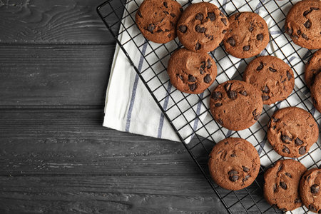 Cooling rack with chocolate chip cookies on wooden background, top view. Space for text