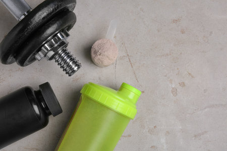 Bottle with protein shake, scoop of powder and dumbbell on gray background, top view. Space for textの写真素材