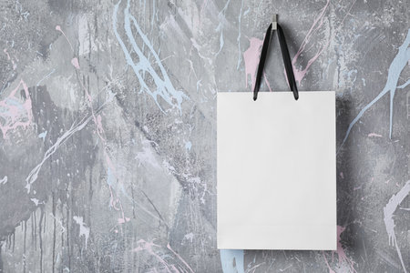 Paper shopping bag with handles hanging on color wall. Mock up designの写真素材