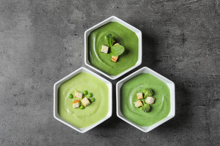 Dishes with different fresh vegetable detox soups made of green peas, broccoli and spinach on table,...