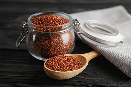 Spoon and jar with red quinoa on black wooden tableの写真素材