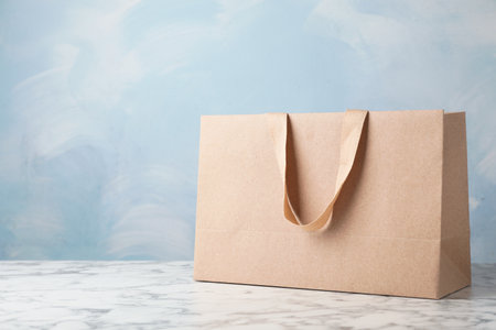 Paper shopping bag with comfortable handles on table against color background. Mockup for designの写真素材