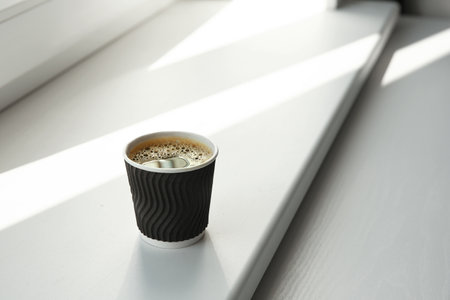 Cardboard cup of coffee on window sill indoorsの写真素材