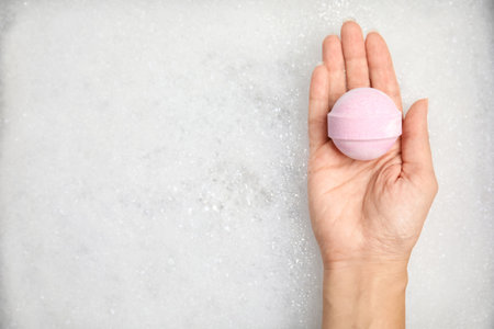 Woman holding bath bomb over foam, top view. Space for textの写真素材