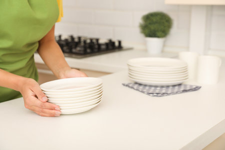 Woman with stack of clean dishes in kitchen, closeupの写真素材