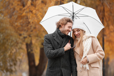 Young romantic couple with umbrella in park on autumn dayの写真素材